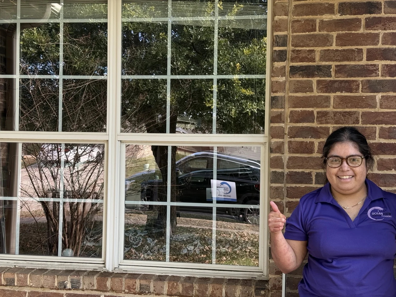 A smiling person in an Oceanview Window Cleaning polo beside a home’s windows