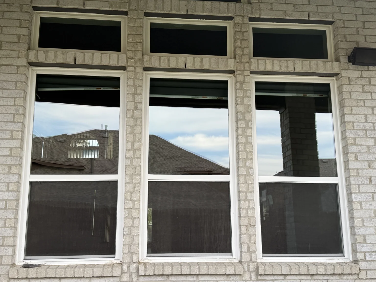 Three tall windows on the front of a white-brick home